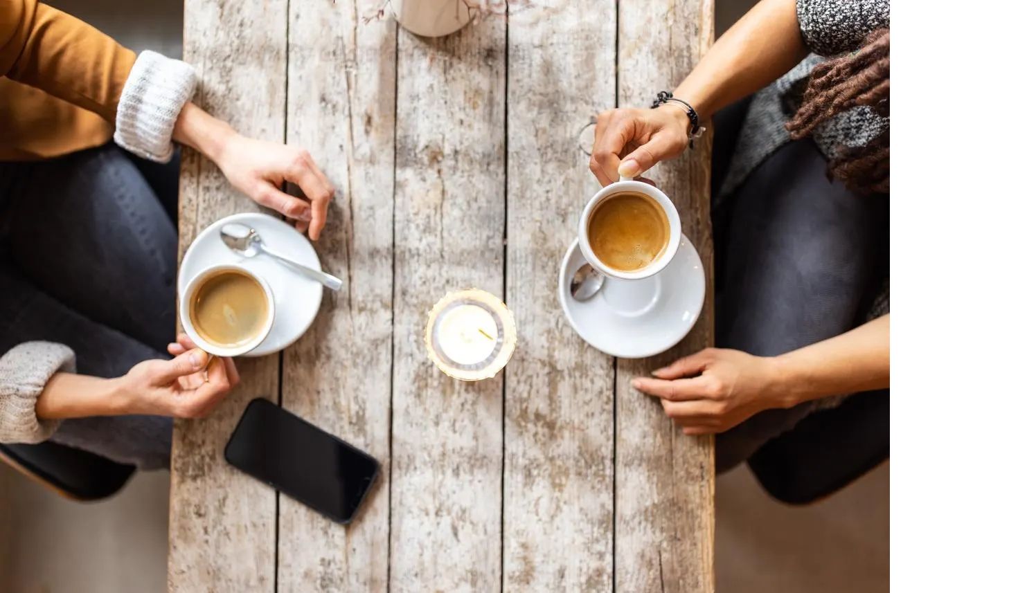 Two people talking across a wooden table, each with a cup of coffee